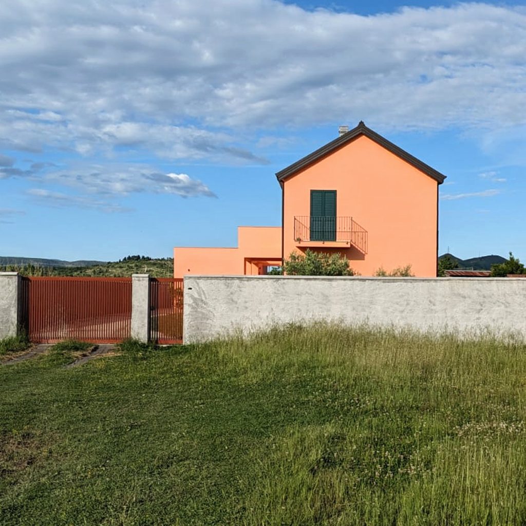 Terrakottafarbenes Einfamilienhaus hinter einer Gartenmauer